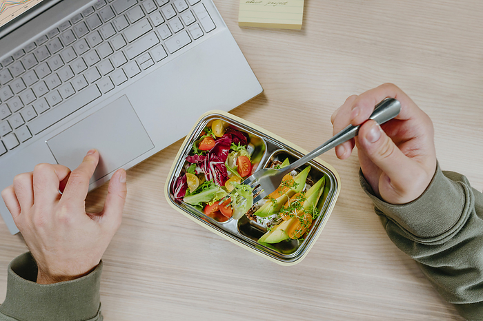 Freelancer working on laptop and having vegetarian food from lunch box