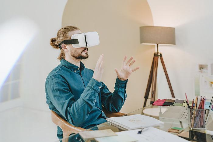 Interior designer wearing VR glasses and sitting on chair at office
