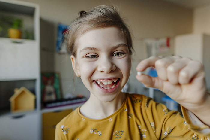 Cheerful girl holding broken tooth at home