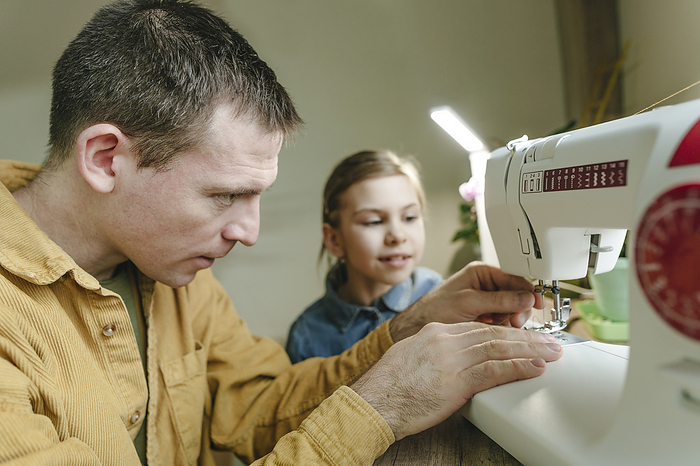 Focused father putting thread on sewing machine needle at home