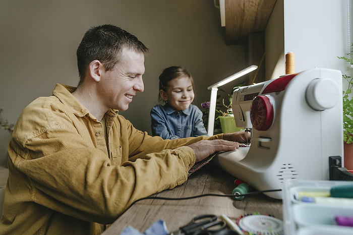 Happy daughter with father sewing recycled clothes through machine at home