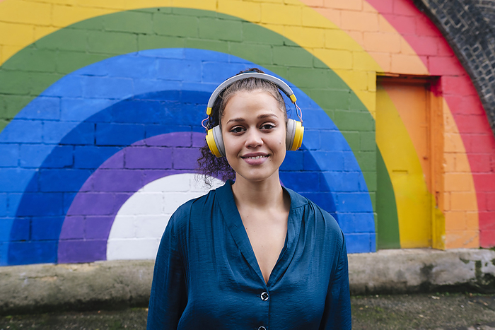 Smiling woman wearing wireless headphones in front of rainbow wall