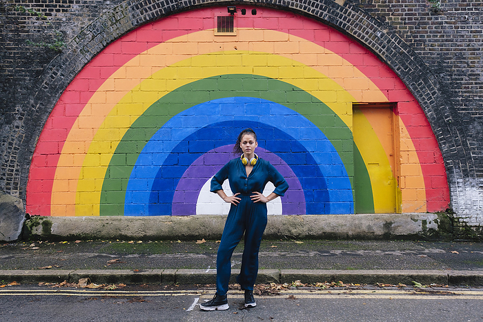Woman standing with hands on hips in front of rainbow wall