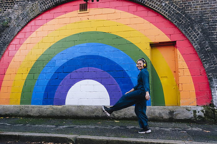Happy woman wearing wireless headphones enjoying in front of rainbow wall