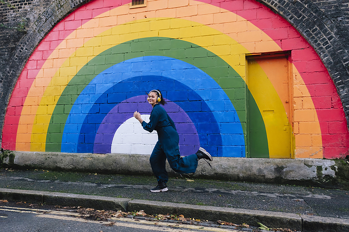 Happy young woman running in front of rainbow wall