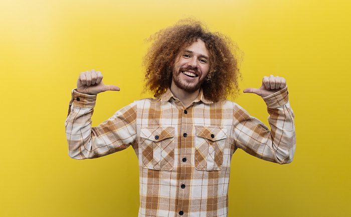 Smiling man showing thumbs down gesture in front of yellow wall