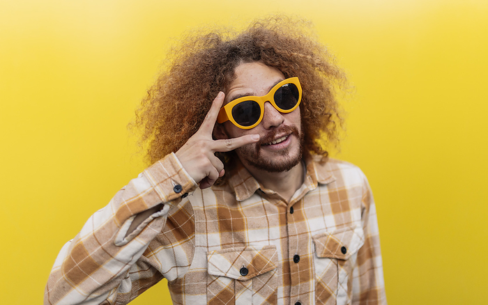 Man wearing sunglasses and showing peace sign in front of yellow wall