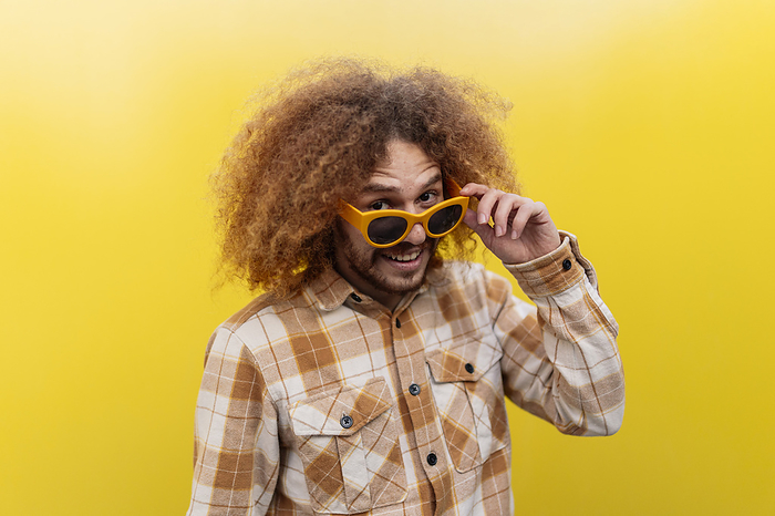 Happy man wearing sunglasses and standing in front of yellow wall