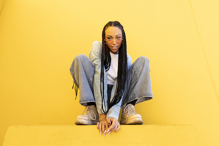 Woman with box braids crouching in front of yellow wall
