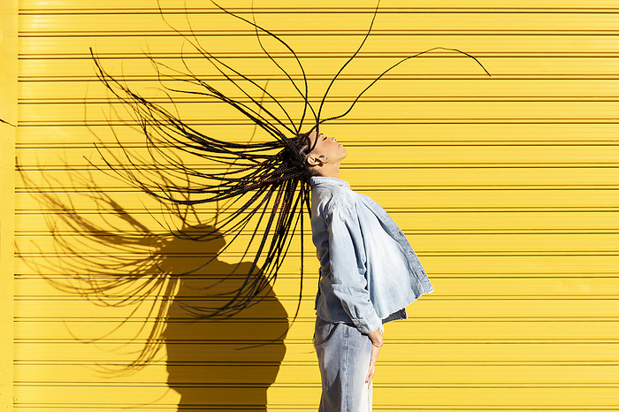 Young woman tossing hair in front of corrugated shutter on sunny day
