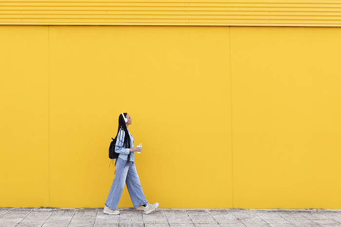 Young woman walking on footpath in front of yellow wall