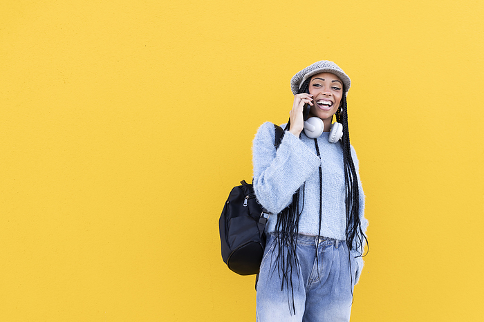 Cheerful woman talking on smart phone in front of yellow wall