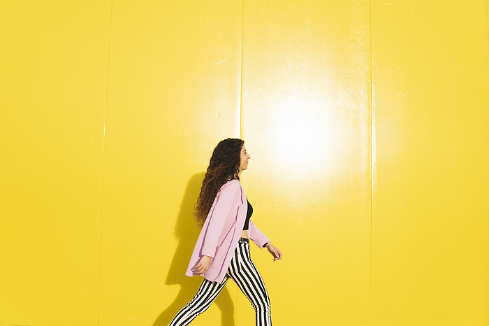 Woman wearing pink jacket and walking against yellow background
