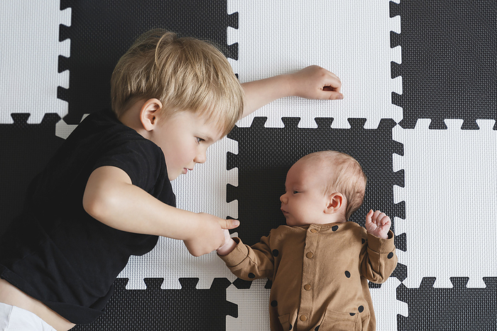 Boy holding baby brother's hand on mat