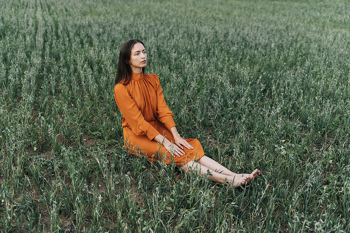 Thoughtful woman sitting amidst crops in corn field