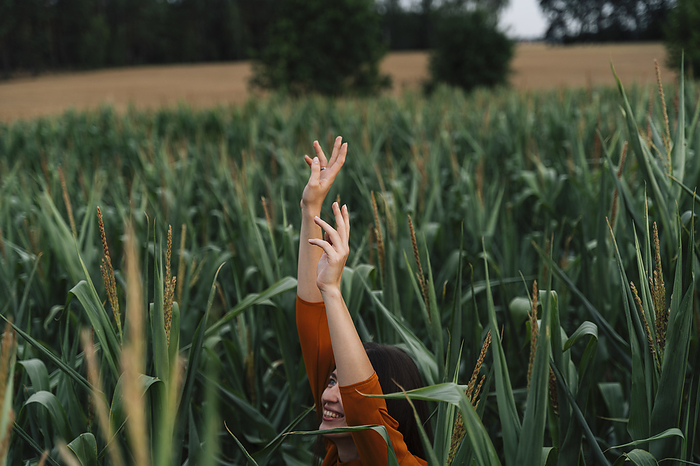 Smiling woman with arms raised having fun amidst corn crops