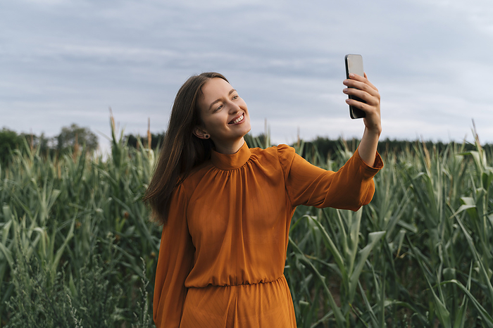 Happy woman taking selfie in front of corn crops at field