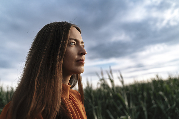 Thoughtful woman in corn field at sunset