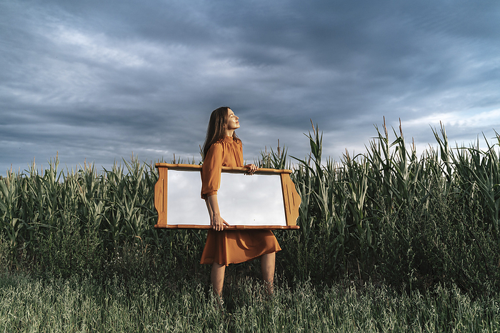 Woman carrying mirror in front of cloud at corn field