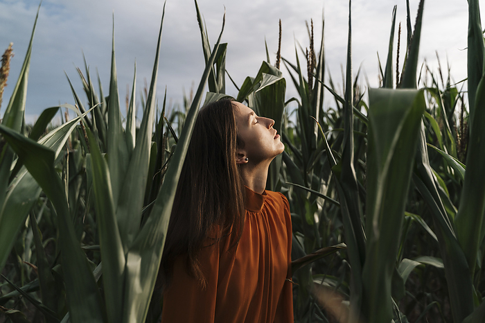 Thoughtful woman with eyes closed amidst corn crops in field