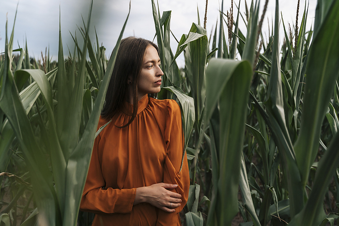 Thoughtful woman standing amidst crops in corn field