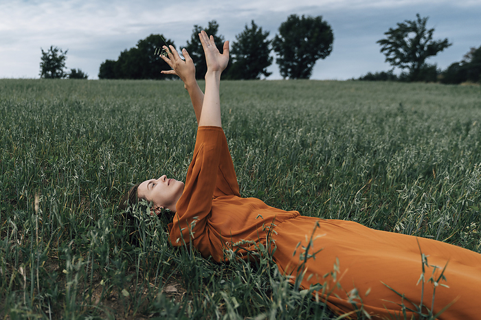 Woman with arms raised lying in corn field