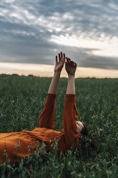 Woman with arms raised lying in field at sunset