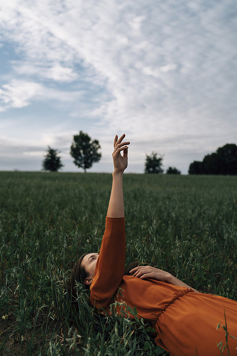 Woman with hand raised lying in field at sunset