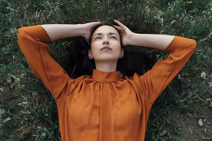 Thoughtful woman with head in hands lying in field