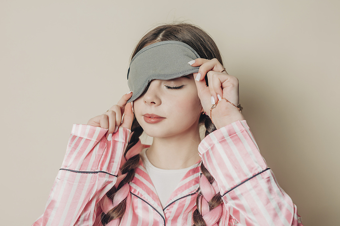 Woman wearing eye mask and pajamas in front of wall
