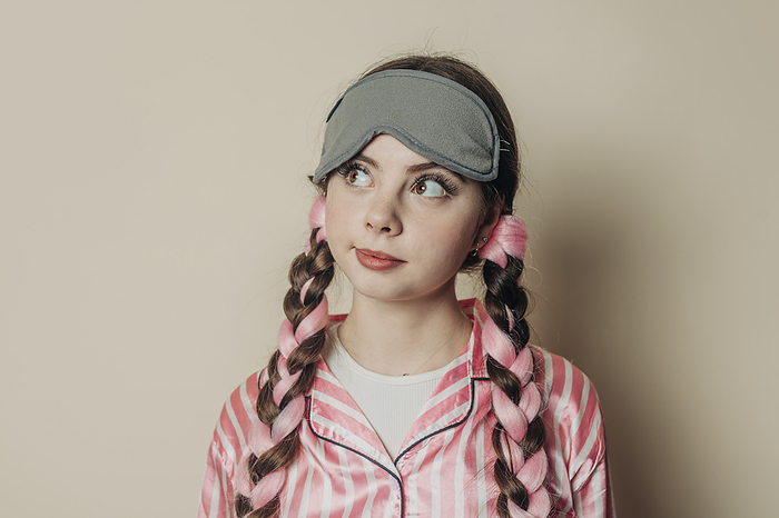 Thoughtful woman wearing eye mask and pajamas in front of wall
