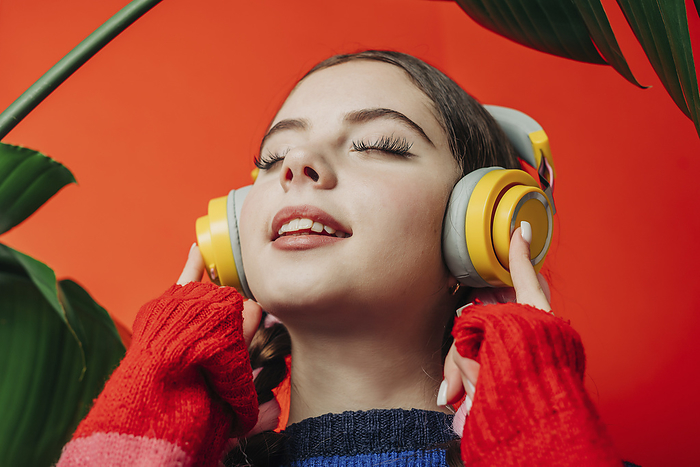 Woman with eyes closed listening to music in front of red wall
