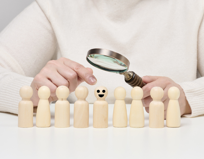 Woman holding a magnifying glass and wooden men on a white table. Personnel recruitment concept, talented employees. Career advancement Woman holding a magnifying glass and wooden men on a white table. Personnel recruitment concept, talented employees. Career advancement