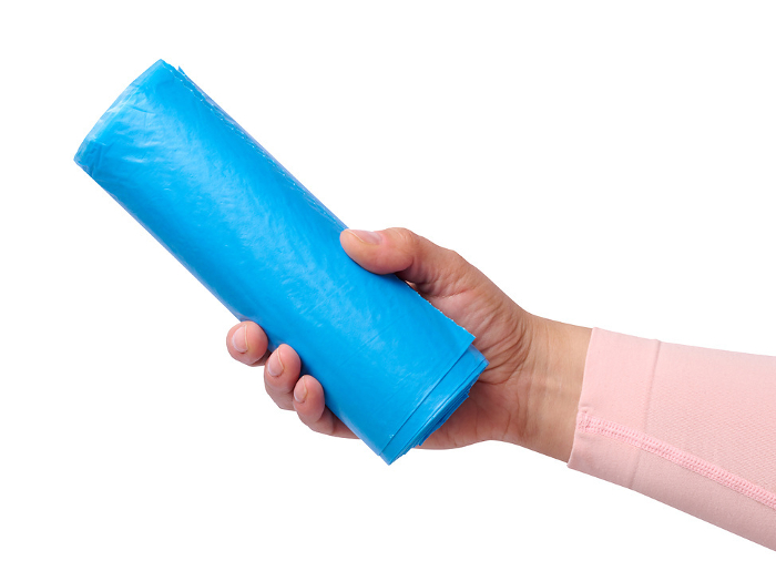 A woman s hand holds a roll of plastic bags for the trash can on a white isolated background A woman s hand holds a roll of plastic bags for the trash can on a white isolated background
