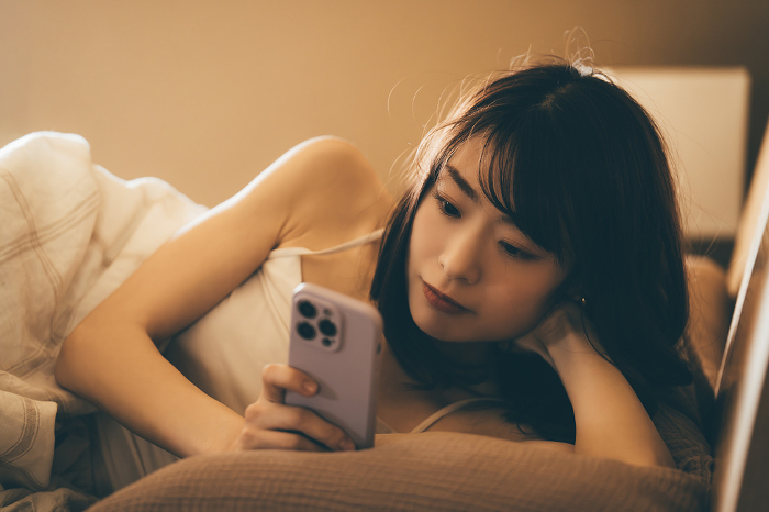 Japanese woman in bed using smartphone (People)