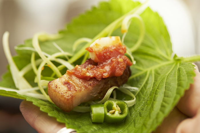 Man's hand wrapping samgyeopsal with egoma leaves