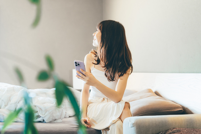 Smiling Japanese woman in bed using smartphone (People)