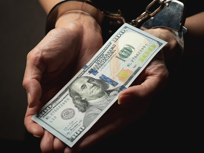 Handcuffed female hand holding a U.S. dollar bill