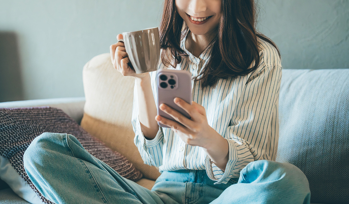 Smiling Japanese woman using her phone on the sofa (People)