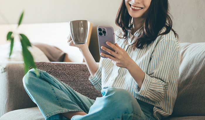 Smiling Japanese woman using her phone on the sofa (People)