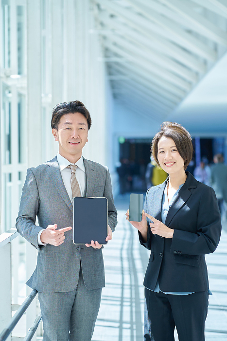 Japanese man and woman in suits holding portable digital communication devices (People)