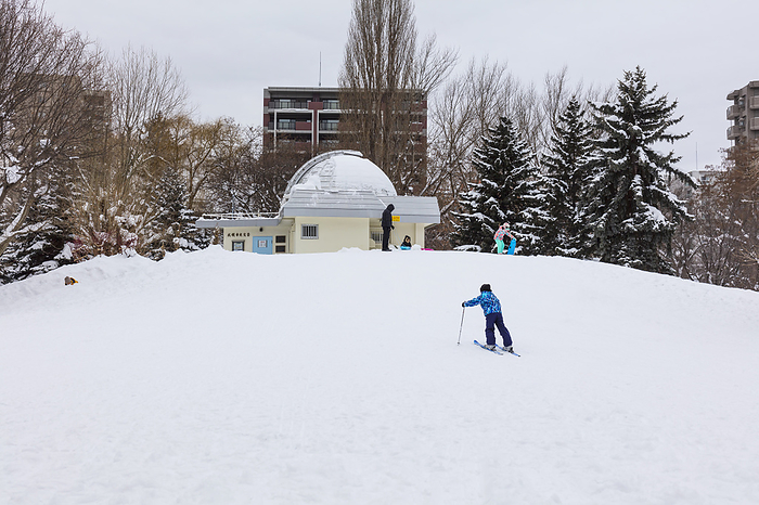 Children playing in the snow with the observatory in Nakajima Park, Hokkaido, Japan