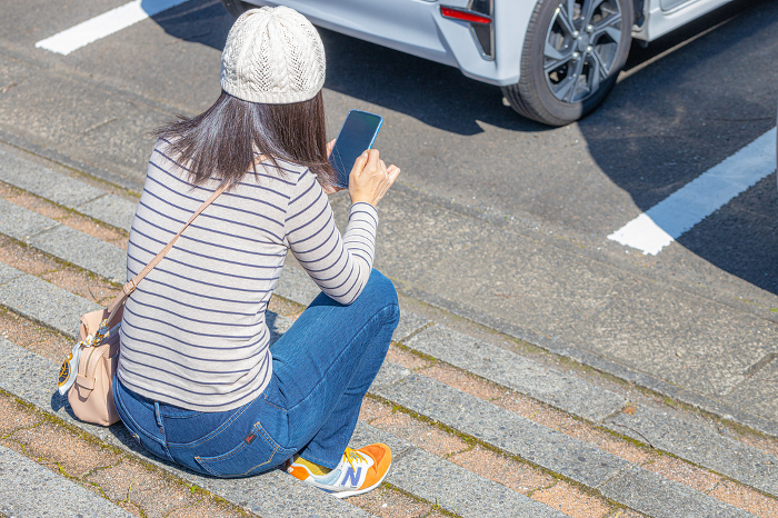 Back view of a woman sitting on the steps of a parking garage operating a smartphone.