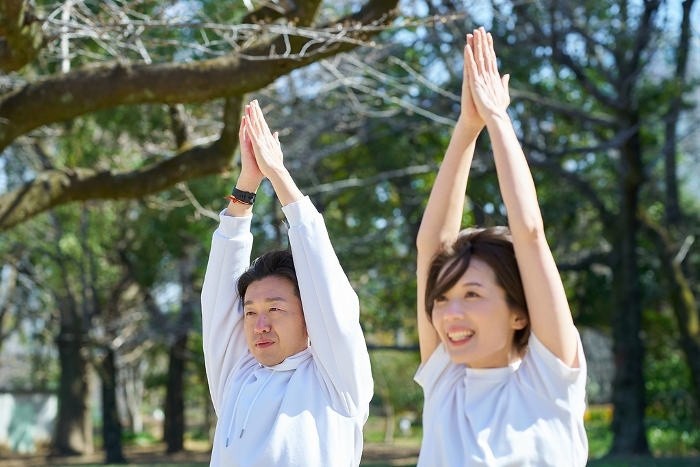 Japanese men and women doing yoga outdoors side by side.