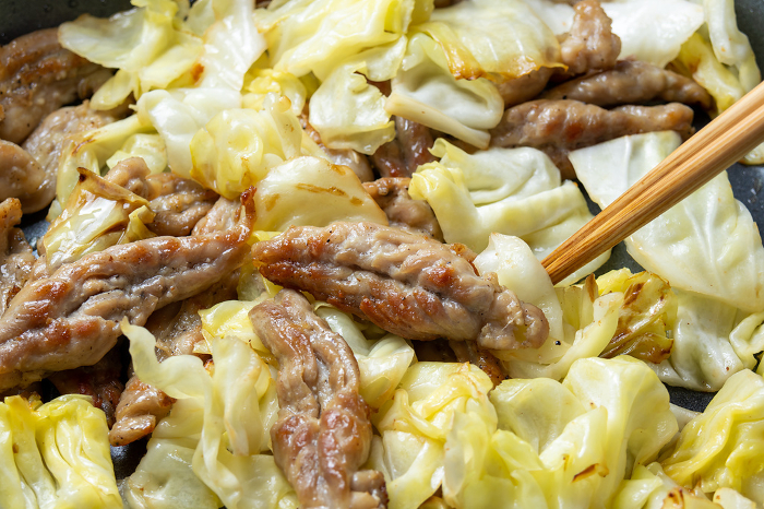 Cooking scene of pan frying chicken (cecelery) and cabbage.