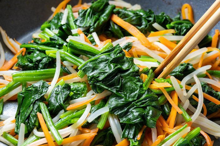 A cooking scene in which vegetables (spinach, carrots, bean sprouts) are pan-fried.