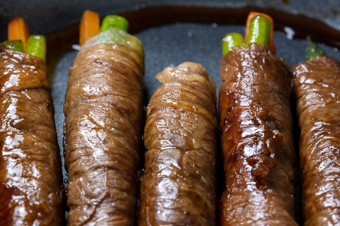 Asparagus and carrots wrapped with beef, cooking scene.