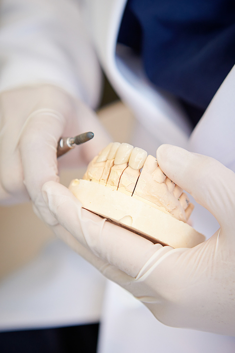 A man's hand shaving a denture at the dental lab bar.