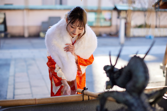 A Japanese woman in a furisode kimono purifies her hands at a hand-watering fountain.
