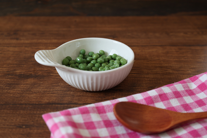 Green peas in a white ceramic bowl on a wooden table